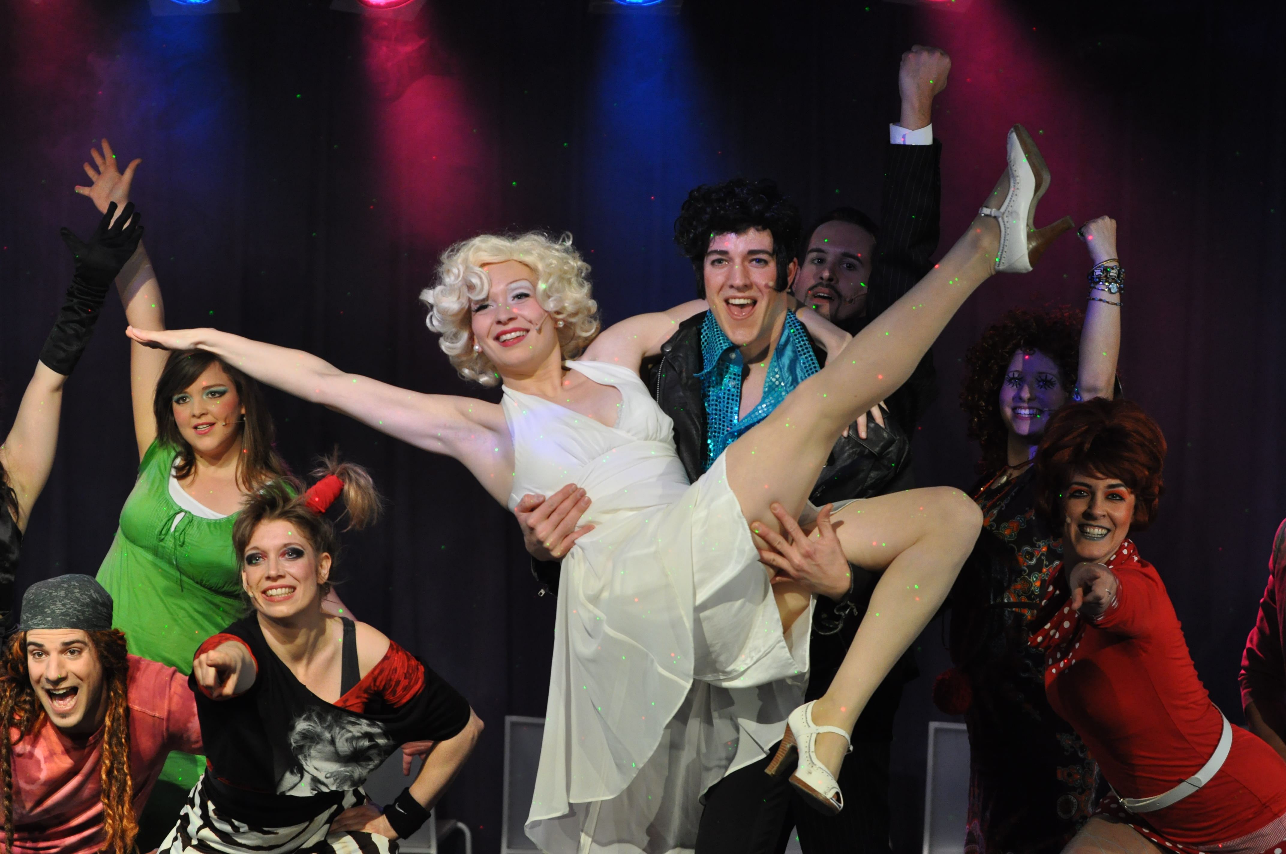 Ein Gruppenfoto des Musical-Ensembles in 2013: Ein nach Elvis Presley aussehender Mann hält eine Schauspielerin, die nach Marilyn Monroe stilisiert wurde, auf den Armen.
